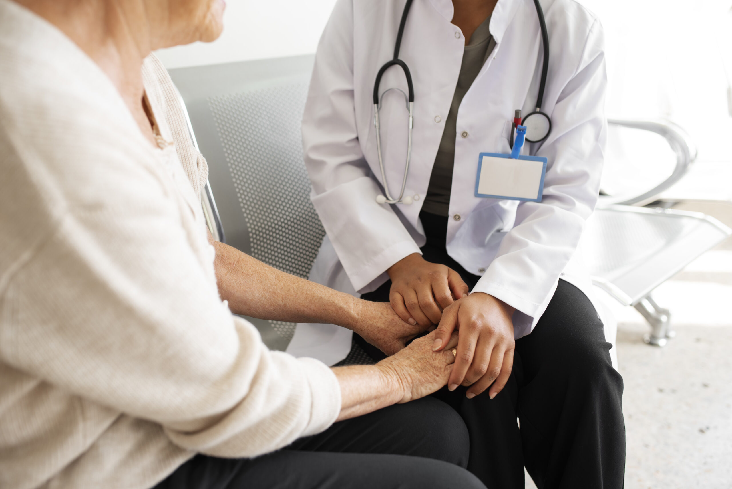 Treating fibromyalgia, image of a doctor wearing a white coat, sitting, and holding a female patient’s hands.