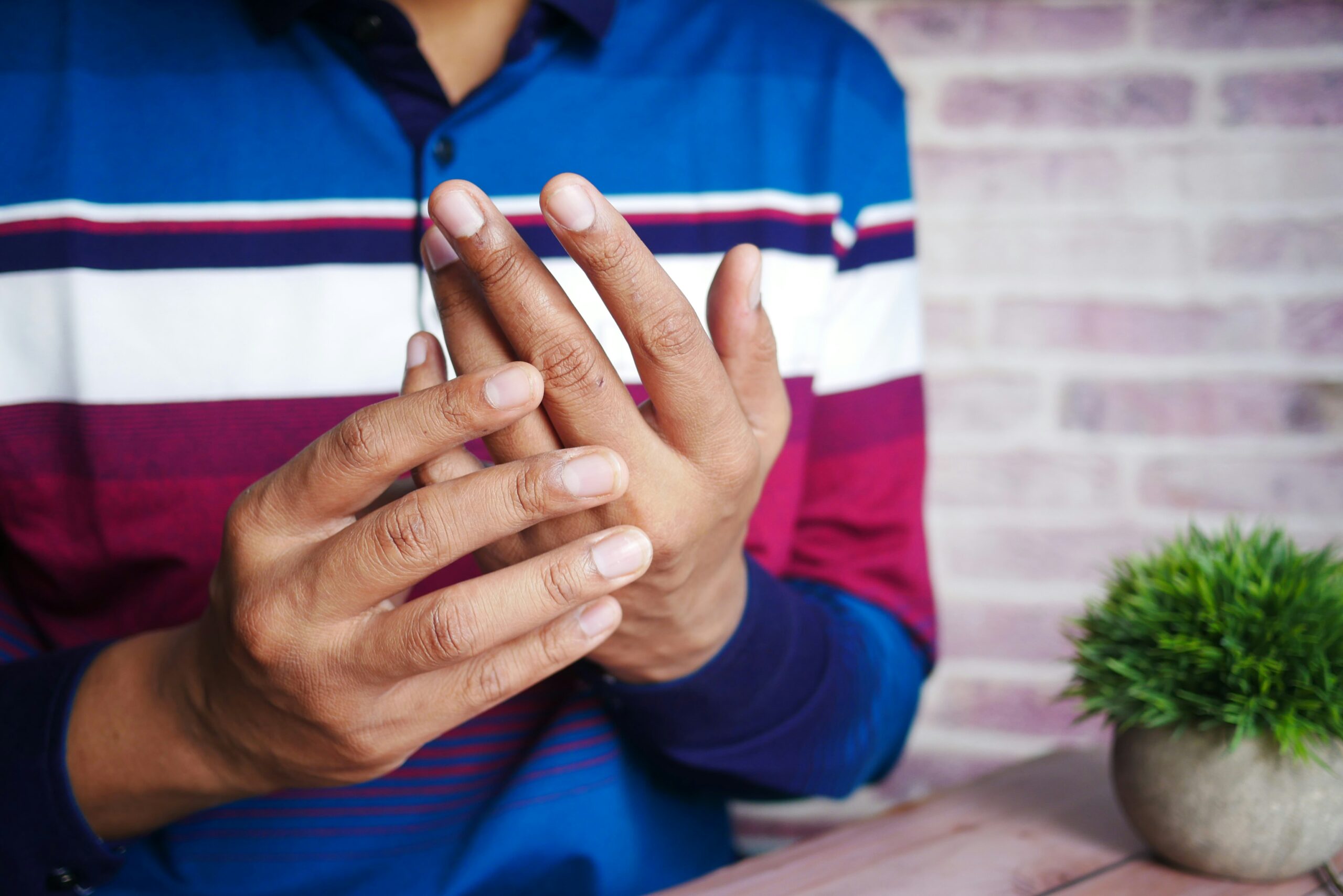 Treating chronic fatigue syndrome, image of a man wearing a striped long sleeve shirt holding his left hand in his right.