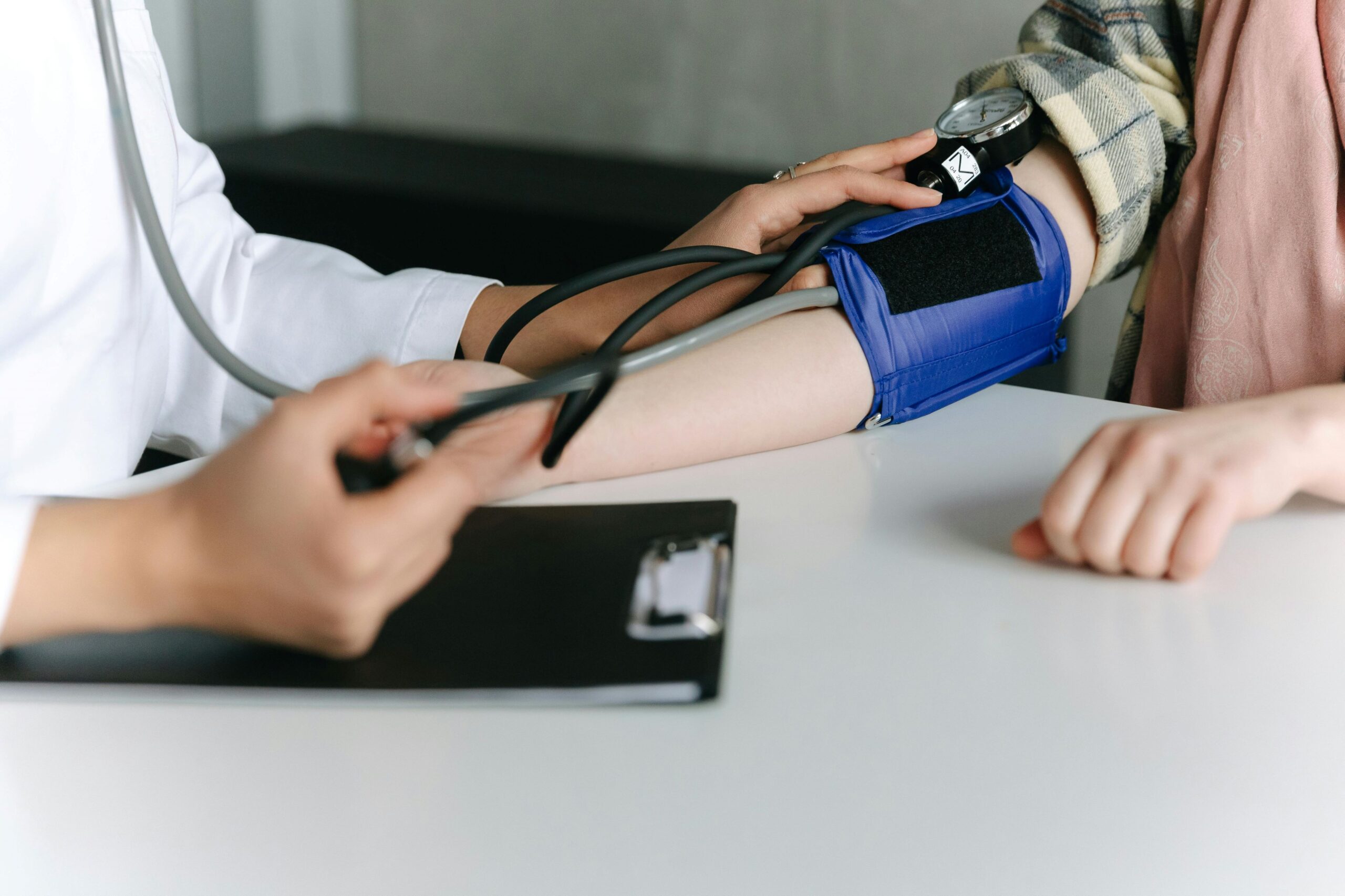 Postural Orthostatic Tachycardia Syndrome, a doctor taking the manual blood pressure of a younger woman on an exam table.