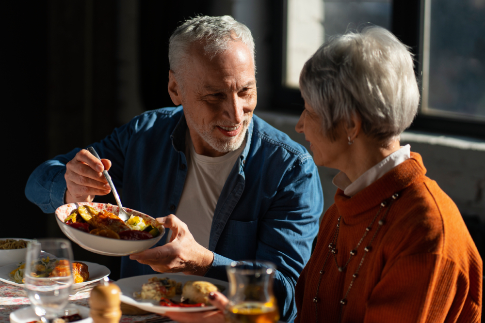 Inflammatory Bowel Disease (IBD), image of an older couple sitting at the kitchen table sharing food with each other.