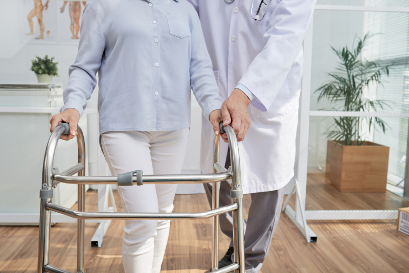 Multiple sclerosis, image of a doctor helping a female patient walk using a walker.