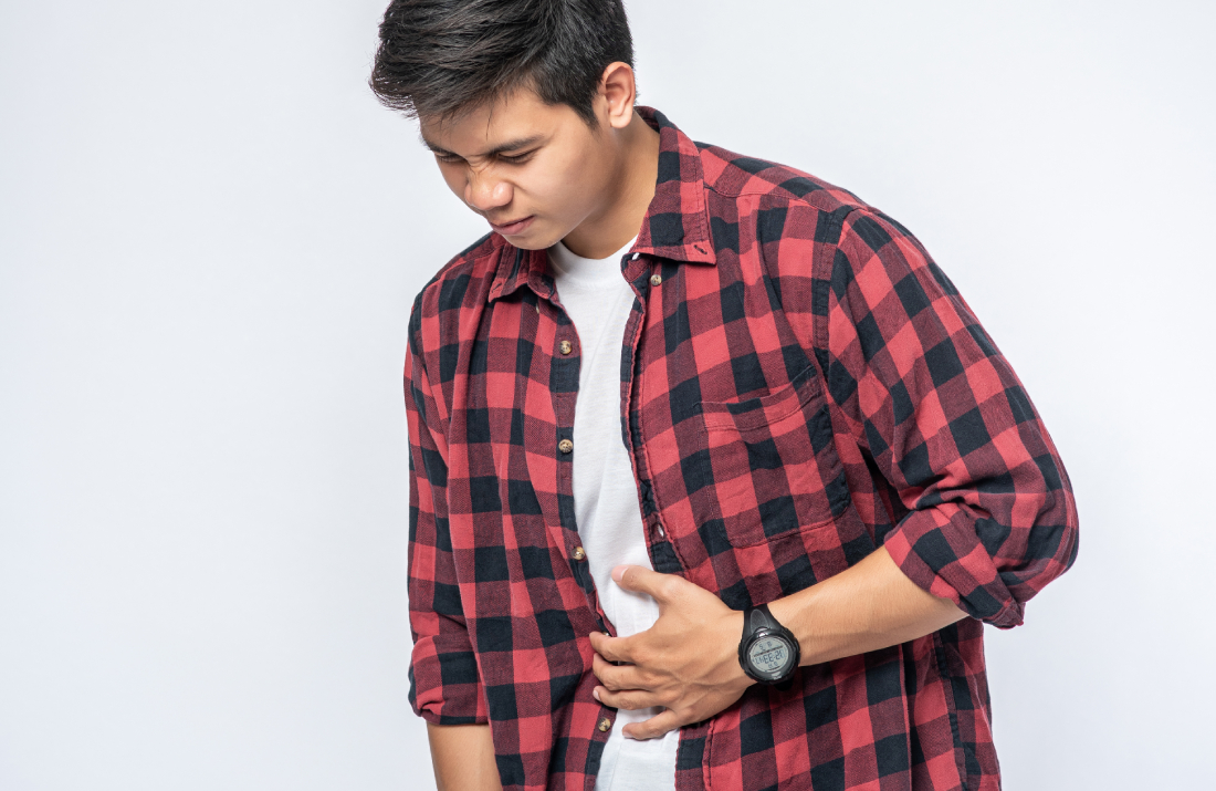 Mast Cell Activation Syndrome, image of a man wearing a red and black plaid flannel shirt holds his stomach with his left hand with a look of pain on his face.