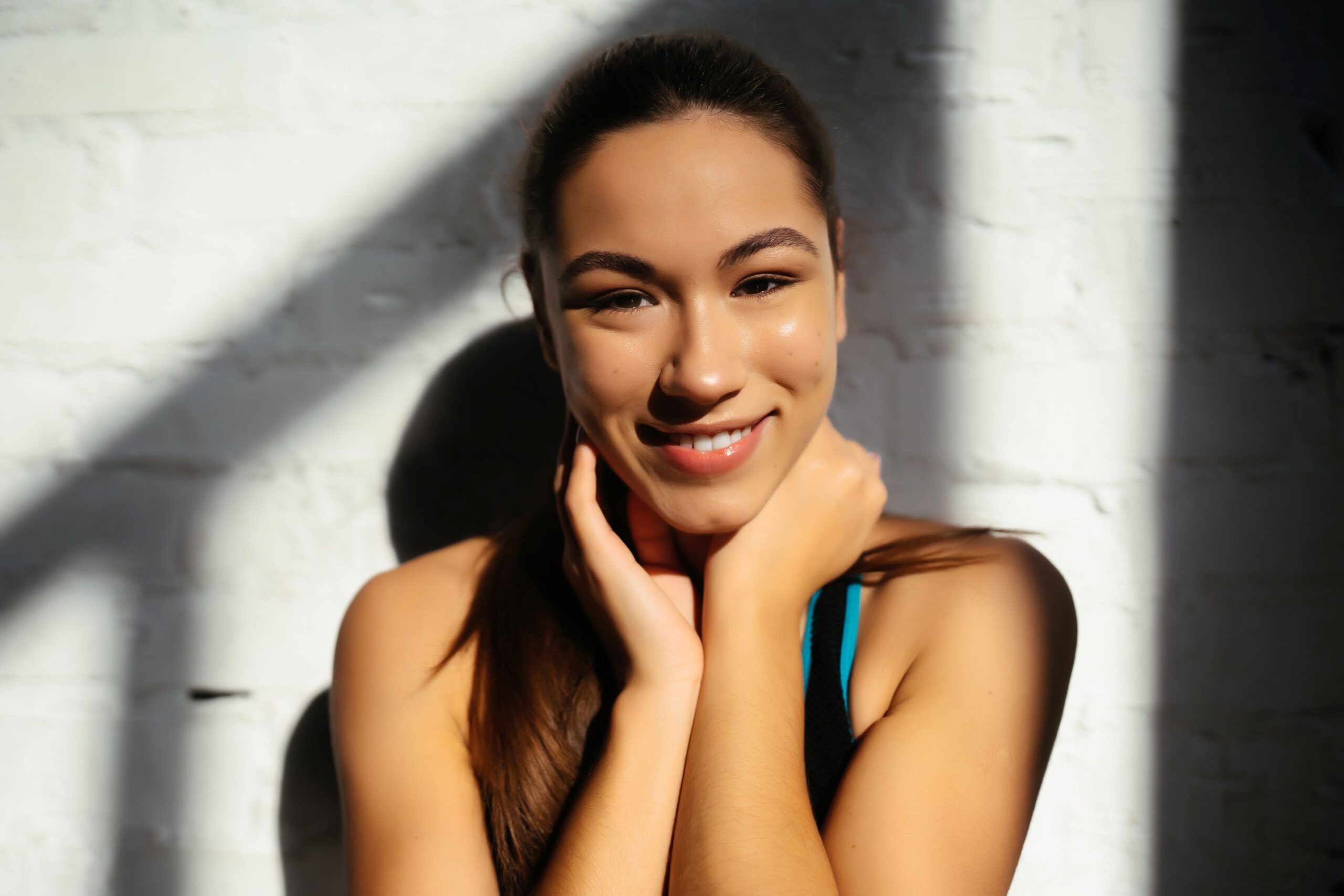 PDRN Therapy, image of a smiling woman with her dark hair pulled back and her hands placed gently around her face.