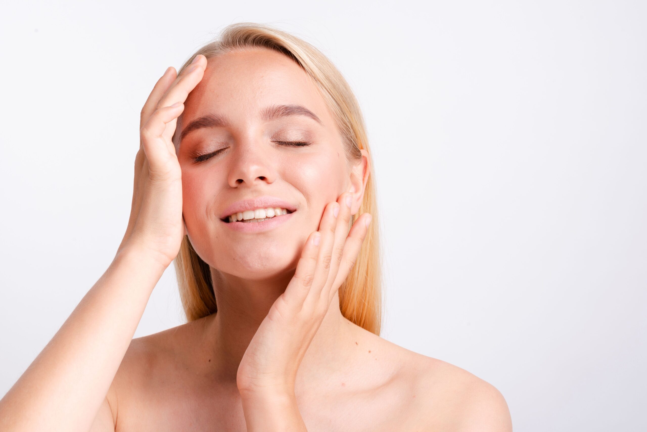 PDRN Therapy, image of a woman with blonde hair, glowing skin and eyes closed with both hands gently placed on her face.