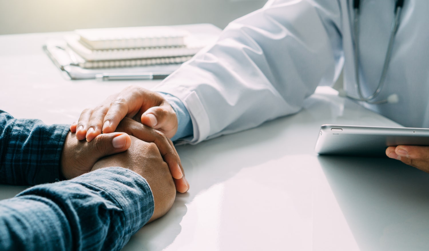 Treating depression, image of a doctor placing his right hand over a male patient’s folded hands.