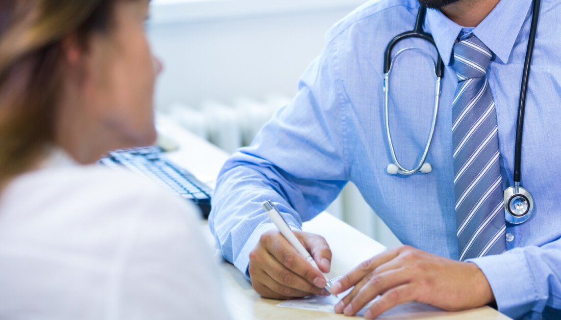 Adrenal Stress, image of a doctor sitting at a desk with a pen in his right hand talking to a female patient wearing a white blouse.