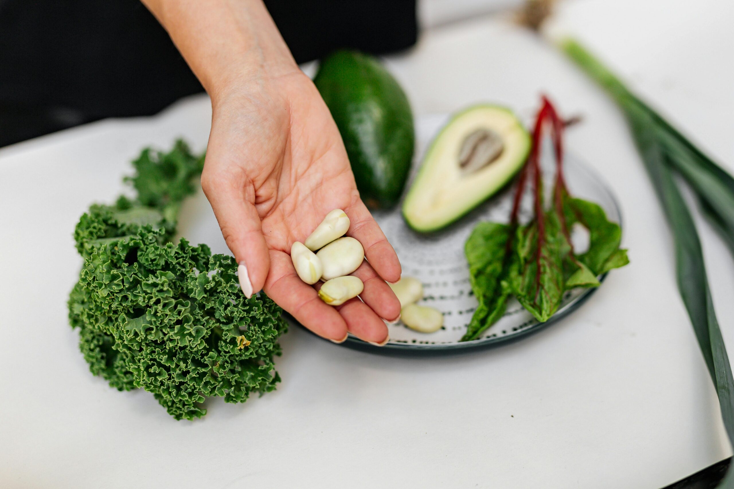 Chronic Inflammatory Response Syndrome (CIRS), image of a woman's hand holding fava beans with a plate of vegetables on the table below